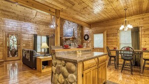 A log cabin interior with a stone fireplace, wooden dining table, and a cozy seating area. - Amazing Luxury Log Cabin! Great Living Space! Mountain Views! 2 Jacuzzi Tubs!  (Sevierville)