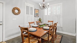A dining room with a wooden table set for six, surrounded by chairs, a chandelier, and a decorative wreath on the wall. - Elegant Downtown Chattanooga Retreat Near Riverfront & UTC  Sleeps 6 Fireplace (Chattanooga)