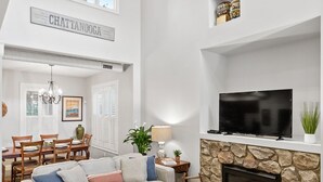 A spacious living room with a fireplace, a television, and a dining area with a chandelier. - Elegant Downtown Chattanooga Retreat Near Riverfront & UTC  Sleeps 6 Fireplace (Chattanooga)