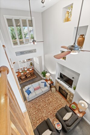 A spacious living area with a high ceiling, a fireplace, a television, and a dining area with a view of the outdoors. - Elegant Downtown Chattanooga Retreat Near Riverfront & UTC Sleeps 6 Fireplace (Chattanooga)