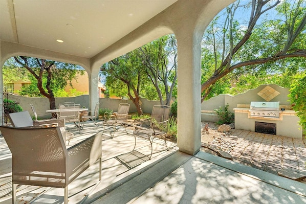 Un patio al aire libre con una parrilla, zona de estar y árboles.