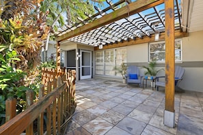 A covered patio area with a wooden pergola, tiled flooring, and outdoor seating.