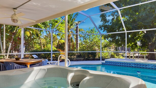 Un espace avec un jacuzzi et une piscine, entouré d’une structure en verre, ainsi qu’une table en bois avec des chaises.