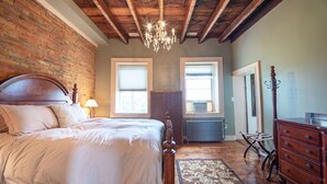 Une chambre avec un grand lit, des poutres apparentes en bois au plafond, un lustre, une commode et un radiateur.