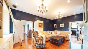 Un salon doté d’un plancher en bois, d’un canapé d’angle beige, d’un fauteuil à bascule et d’une table basse de couleur foncée.