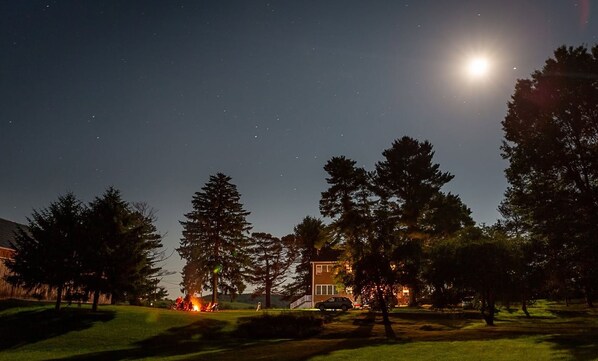 A nighttime view of a residential area with a house, trees, and a visible fire in the distance. - Restored colonial farmhouse near Seven Springs -- Perfect for family gatherings (Somerset)
