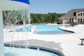 A swimming pool with a water fountain feature, surrounded by lounge chairs and a building with a sloped roof. - Minutes from Bethany Beach Boardwalk! (Millville)