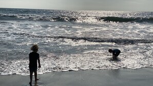 Ein Strand mit Wellen und zwei spielenden Kindern im Wasser.