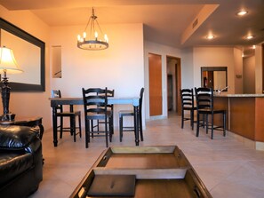 A dining area with a table, chairs, and a chandelier. There is a sofa and a tray table in the foreground.