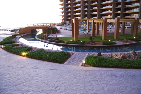 Un resort con piscina, una zona cubierta con sillones de descanso y un edificio con varios balcones.