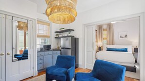 Een moderne slaapkamer met een groot bed, twee blauwe fauteuils, een zithoek met een keuken, en een groot raam.