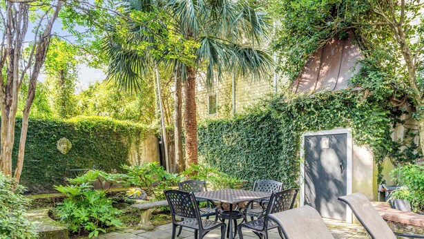 Een terras met een tafel en stoelen, omgeven door weelderige begroeiing en een stenen muur.
