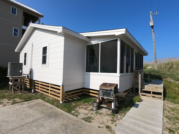 A small, single-story house with a white exterior, a large window, and a small porch. - Tangerine Dreams in South Nags Head Ocean Front (Nags Head)