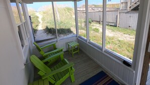 Eine überdachte Veranda mit Blick auf einen sandigen Weg und einen Holzzaun.