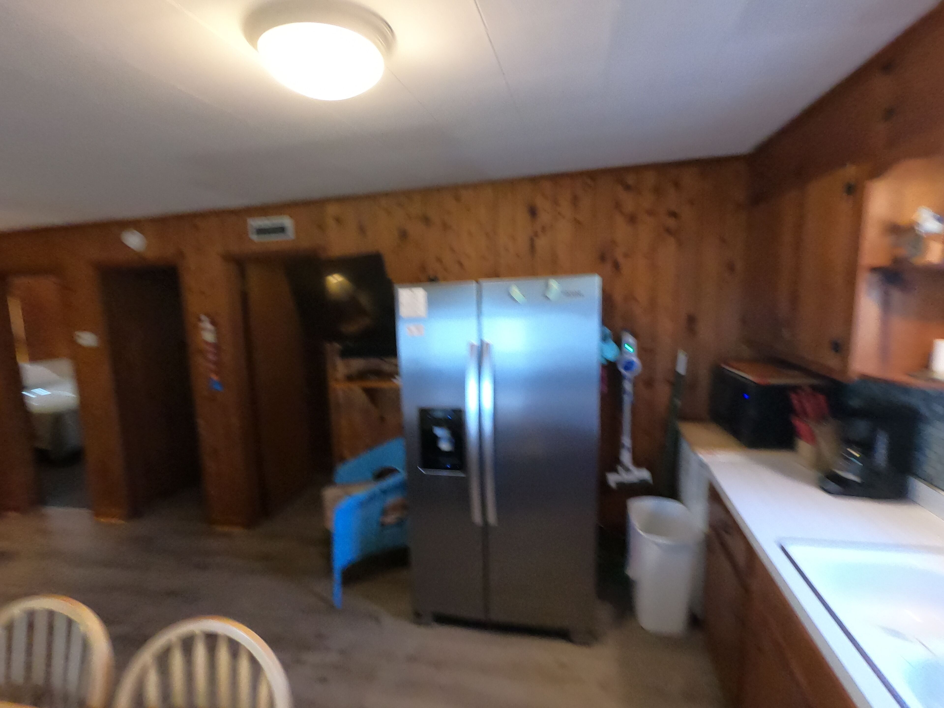 A kitchen with wooden walls, a stainless steel refrigerator, a sink, and a blue chair.