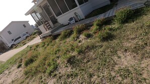 Ein zweistöckiges Haus mit überdachter Veranda und einem kleinen Garten mit roten Blüten.