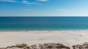 A beach with a clear view of the ocean and a person walking on the sand.