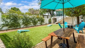 A patio with a wooden table and chairs, a turquoise umbrella, and a small lawn. - Beautiful Home in Old Town Cottonwood WALK to Wine Tasting Rooms & Restaurants! (Cottonwood)
