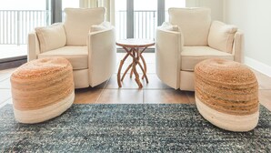 Ein modernes Wohnzimmer mit zwei beigefarbenen Sofas, einem kleinen runden Holztisch und zwei gewebten Hocker.