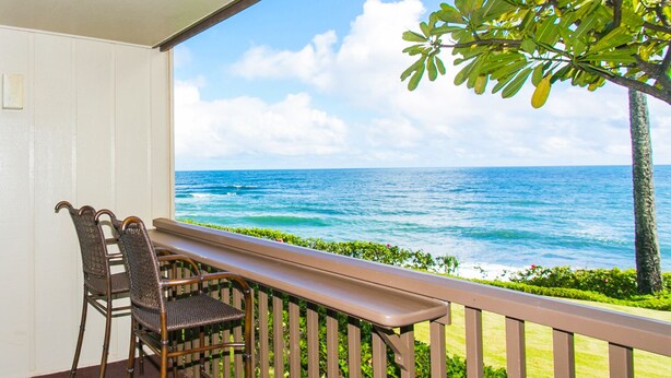 Een balkon met uitzicht op de oceaan, twee rieten stoelen en een houten tafel.