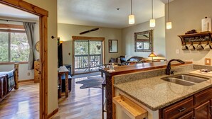 A kitchen with granite countertops, a double sink, wooden cabinets, and a dining area with a table and chairs.