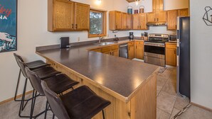 A kitchen with wooden cabinets, a large island with bar stools, stainless steel appliances, and a window with natural light. - Beautifully decorated home w/fireplace & community hot tub/pool/sauna - Hidden Village Getaway (Gallatin Gateway)