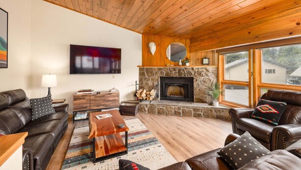 A cozy living room with a stone fireplace, leather sofas, a coffee table, and a large window. - Beautifully decorated home w/fireplace & community hot tub/pool/sauna - Hidden Village Getaway (Gallatin Gateway)
