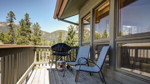 A wooden deck with two chairs and a grill, overlooking a mountainous landscape. - Beautifully decorated home w/fireplace & community hot tub/pool/sauna - Hidden Village Getaway (Gallatin Gateway)