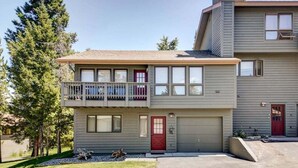 A two-story building with a balcony, a garage, and a red door. - Beautifully decorated home w/fireplace & community hot tub/pool/sauna - Hidden Village Getaway (Gallatin Gateway)