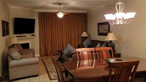 A living room with a flat-screen TV, a sofa, a dining table with chairs, a chandelier, and a patterned rug. -  Luxury Designer 3/2 Condo! Come Relax & Unwind, and Enjoy!!! (Pigeon Forge)