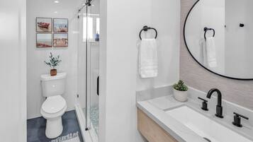 Une salle de bain moderne équipée de toilettes, d’une douche, d’un lavabo et d’un grand miroir.