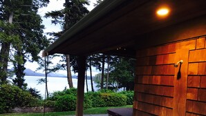 Un bâtiment moderne à l’extérieur en bois, avec un chemin en béton et une vue sur un lac et des montagnes en arrière-plan.