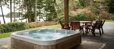 A hot tub with a wooden exterior, surrounded by a wooden deck and a table with chairs.