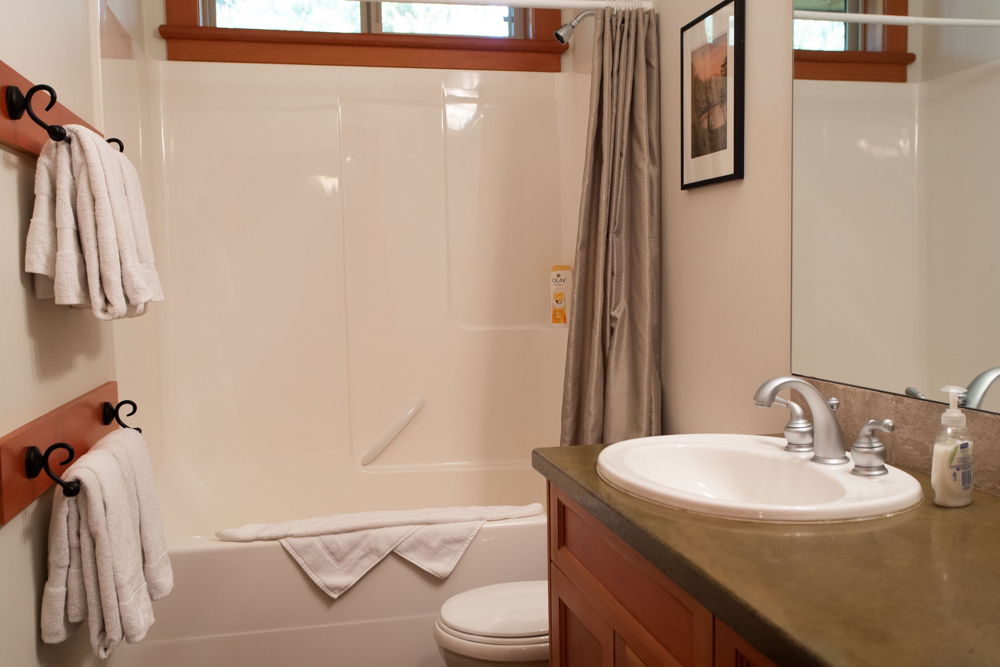 A bathroom with a bathtub, toilet, and sink. There are towels hanging on hooks and a shower curtain.