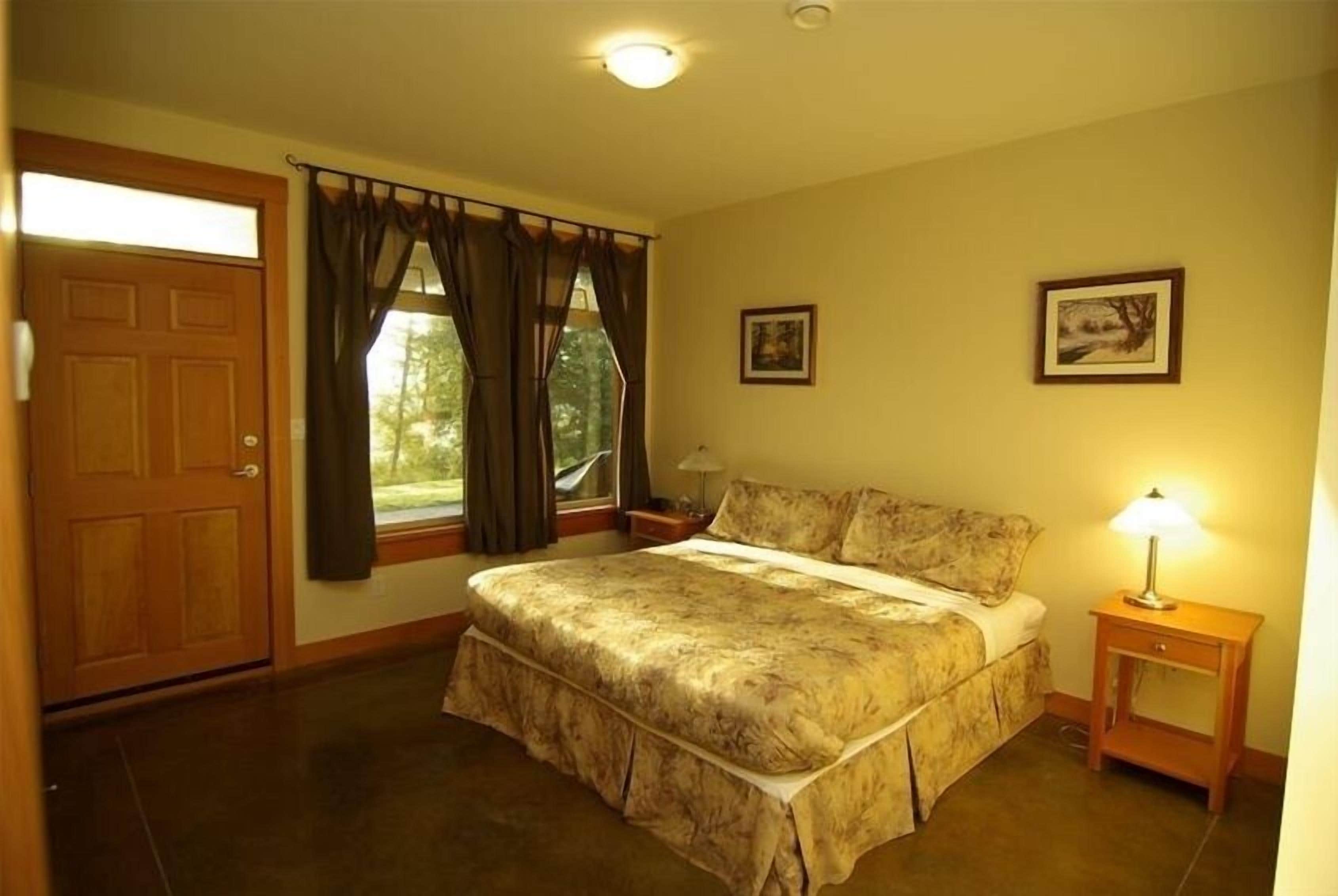 Un dormitorio con una cama grande, una mesita de noche, una ventana con cortinas y una puerta.
