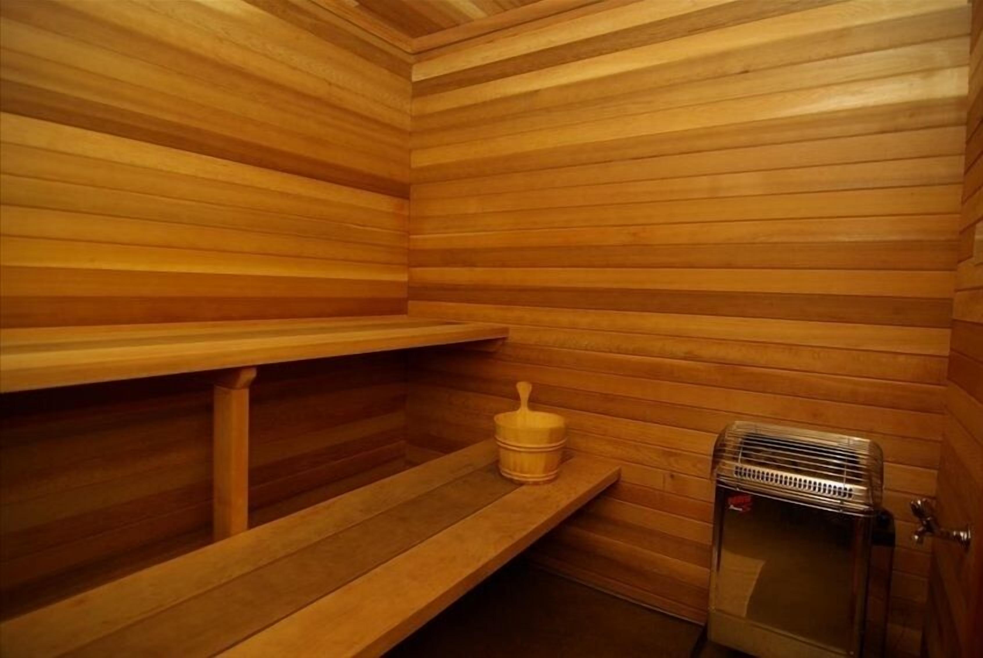 Un sauna avec des murs et des bancs en bois, un petit radiateur et un récipient en bois.