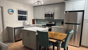 A modern kitchen with grey cabinets, stainless steel appliances, a wooden dining table, and teal chairs. - Freshly renovated Treasure Island Condo in 2025! Close to everything! (Treasure Island)