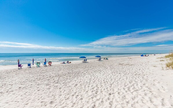 Una playa con arena blanca, varias sillas de playa y sombrillas.