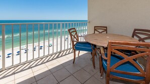 Un balcon donnant sur la plage, une table ronde et deux chaises avec des coussins bleus.