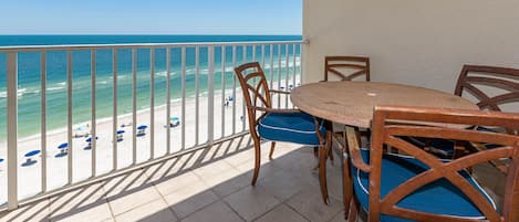 Un balcón con vista a la playa, una mesa redonda y dos sillas con cojines azules.
