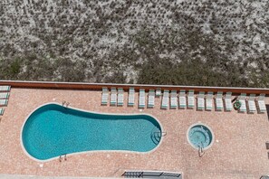 An aerial view of a swimming pool with lounge chairs and a hot tub, surrounded by a brick patio and a natural landscape.
