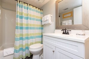 A bathroom with a striped shower curtain, a toilet, a sink with a mirror, and a towel rack.
