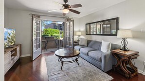 Un salon comprenant un canapé, une table basse et un ventilateur de plafond. Une porte donne accès à un espace extérieur aménagé avec une table et des chaises.