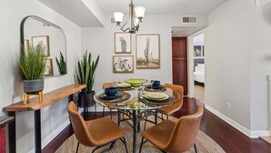Un coin repas comprenant une table ronde en verre, quatre chaises marron, un lustre et des œuvres d’art encadrées accrochées aux murs.