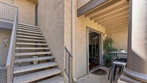Un escalier menant à une porte, un petit espace extérieur aménagé avec une table et des chaises, et une plante en pot.