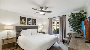 Une chambre d’hôtel avec un lit, un ventilateur de plafond, un bureau avec une télévision, une plante et une fenêtre avec des rideaux.
