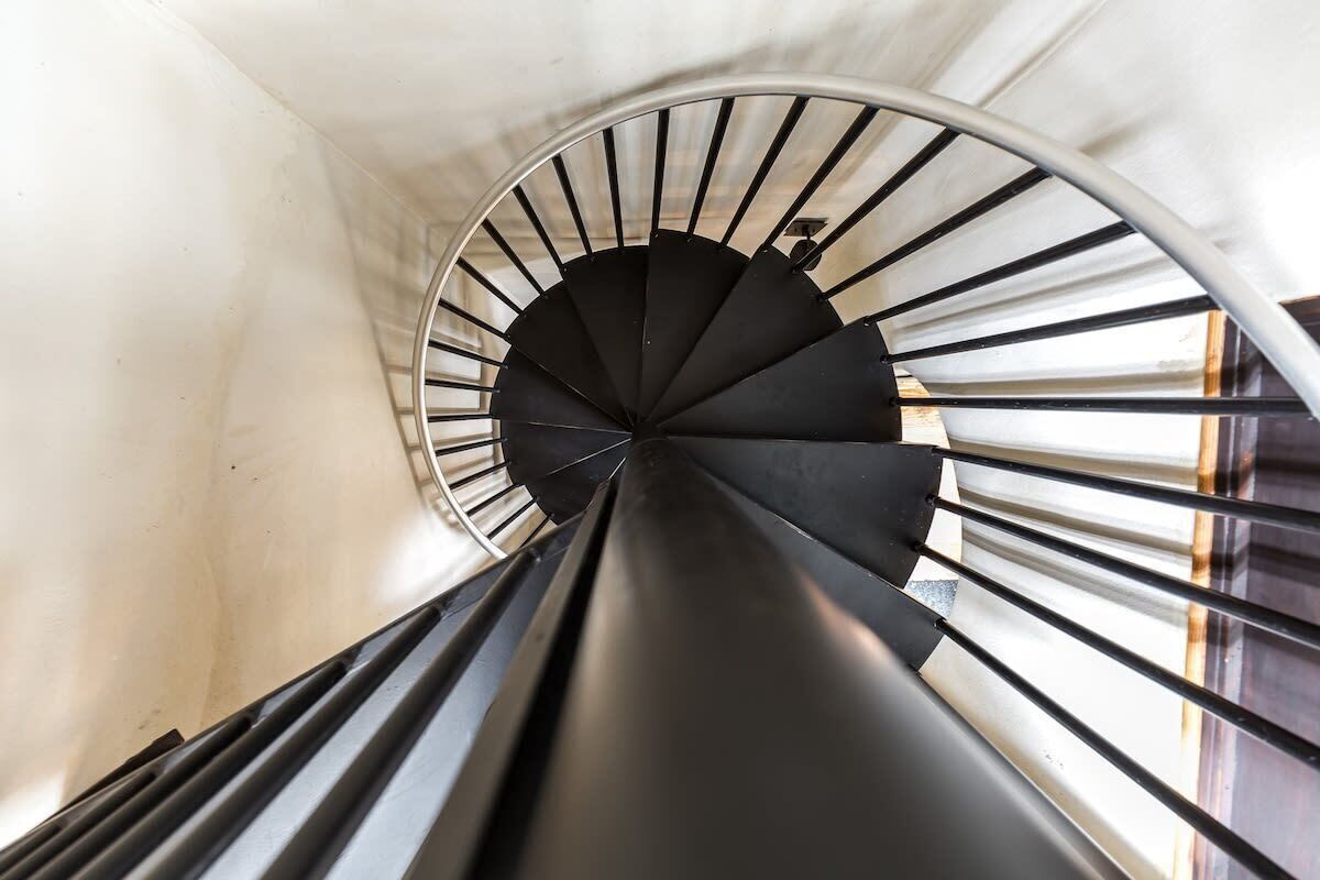 A spiral staircase with a black handrail and white walls.