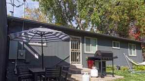 Un patio con una mesa, sillas, una parrilla y tanques de propano.