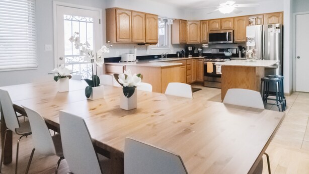 Una cocina moderna con armarios de madera, electrodomésticos de acero inoxidable y una amplia mesa de comedor con sillas.