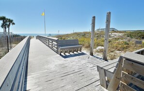 Un muelle de madera que lleva a un banco con vista a la playa y las dunas.